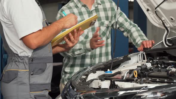 Mechanic Filling Papers While Talking To Car Owner