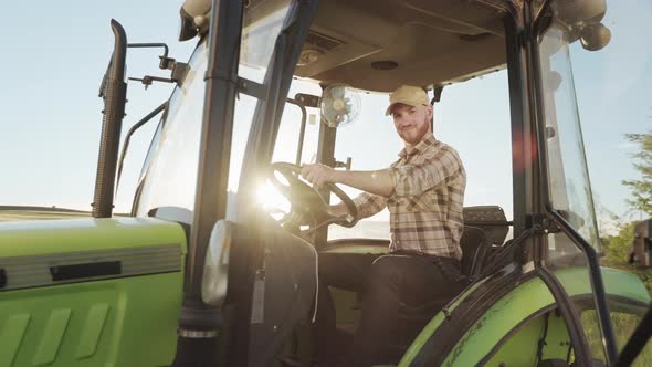 A Young Farmer is Sitting at the Wheel of a Tractor