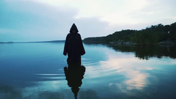 Scary figure in black mantle in the river. Halloween costume.