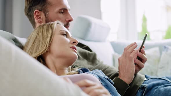 Bored couple using mobile phone and lying on sofa