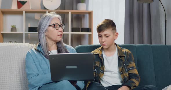 Senior Granny in Glasses Sitting Together with Her Grandson and Him Homework on Computer