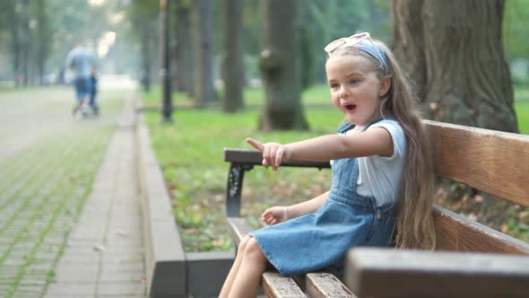 Small Happy Child Girl Sitting on a Bench Resting in Summer Park