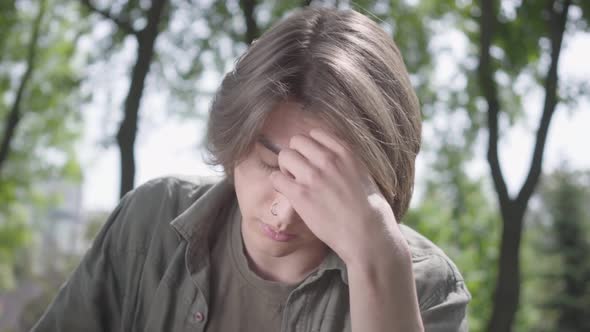 Portrait of a Lonely Depressed Sad Young Man with the Piercing in His Nose Sitting in the Park. The