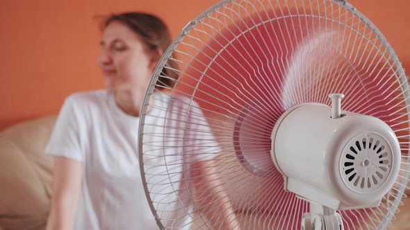 Young Woman Sits in Front of Electric Home Fan Air Stream Blowing Short Hair