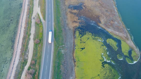 Aerial View of Two Cars Driving on a Dam Highway Surrounded By Lakes at Sunset