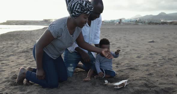 African parents and little son having fun with wood airplane on the beach