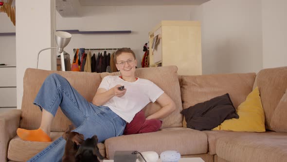 Young Caucasian Happy Woman in a White Tshirt and Blue Jeans Jump on the Sofa to See Tv