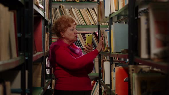 An Elderly Woman Takes a Photo with Books in the Library