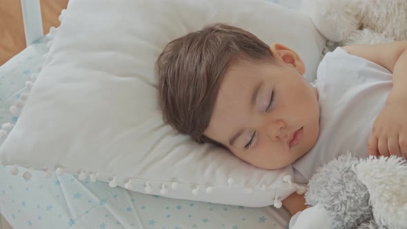 Baby Boy Sleeping In A White Children's Bed With Toy Bear