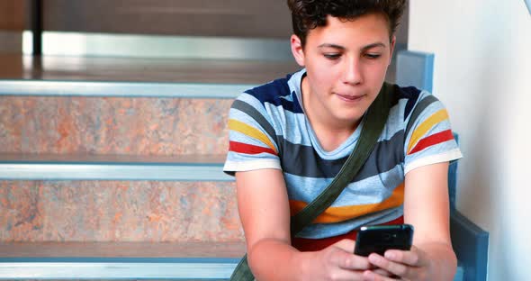 Schoolboy sitting on staircase and using mobile phone