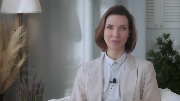 Smiling young woman, blogger, vlogger, influencer, sitting at home, talking, looking at the camera