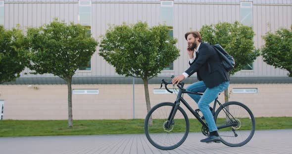 Bearded Man in Stylish Clothes Which Riding a Bike and Has Positive Phone Conversation