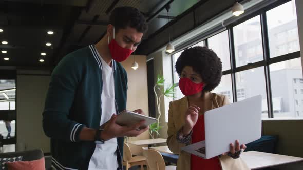 Diverse business people standing using a laptop and a digital tablet in a modern office