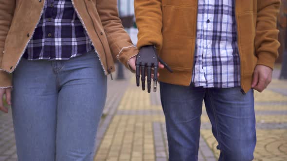 Young Man with a Cyber Prosthetic Arm Holds the Hand of His Beloved Close Up