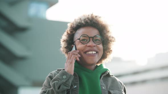 Smiling adult African woman wearing casual clothes talking by phone