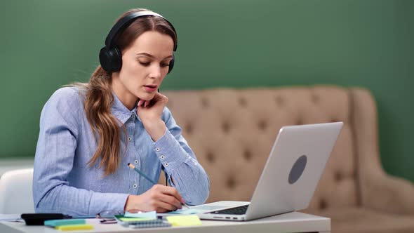 Focused Business Woman in Headphones Making Notes Online Video Call