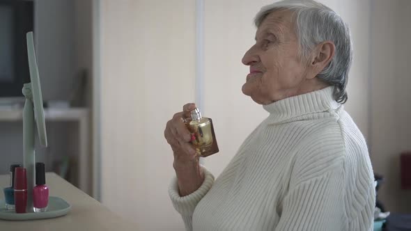 Smiling senior woman spraying perfume in front of mirror, body care, closeup