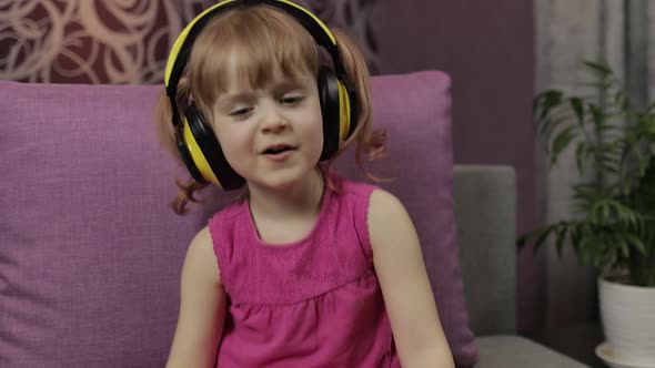 Little Child Girl in Headphones Enjoying Listen Music. Dancing on Sofa at Home