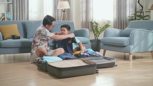 Dad And Son Packing Clothes In Suitcase At Home, Preparing For Their Vacation