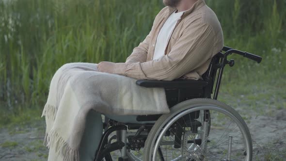 Unrecognizable Man with Injured Legs Sitting on Wheelchair Outdoors and Thinking. Side View of