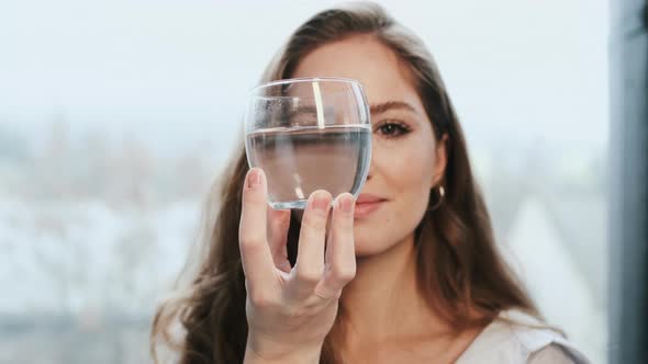 Young Girl With Long Hair Looks Through Glass Of Clear Water.