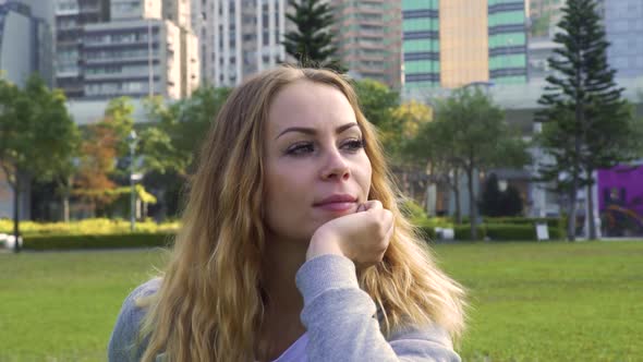 Attractive Lady Sits on Lush Meadow in Picturesque City Park