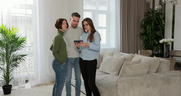 Woman Real Estate Agent Showing Young Couple Apartment Plan Using Tablet