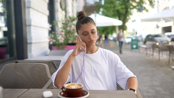 Beautiful Young Woman Sitting in Street Cafe Talking on a Smartphone