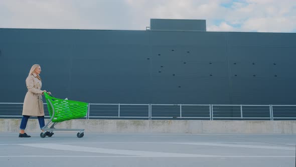 The Happy Woman Is Walking From the Supermarket with Purchases in the Cart