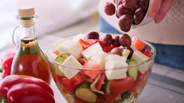 Greek Salad Preparation Series Concept  Woman Pouring Olives Into Bowl with Chopped Vegetables