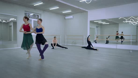 Two Agile Slim Ballerinas Rehearsing Simultaneous Steps Pirouette with Ballet Dancers Warming Up at