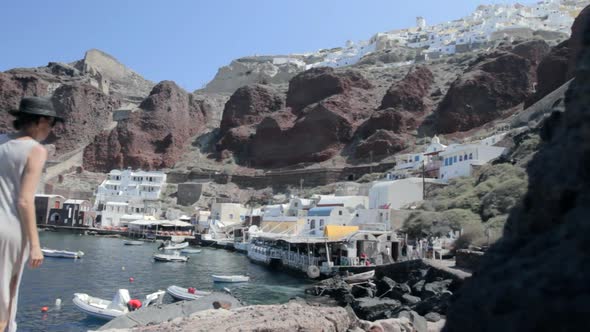 View of a small fishing harbor on a Greek island with a woman that strolls by the rocks.