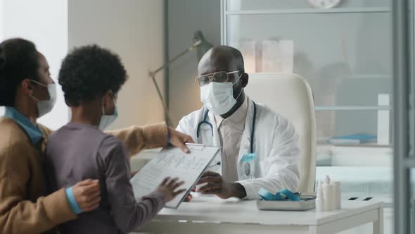 Black Pediatrician in Mask Giving Consultation to Boy and His Mother