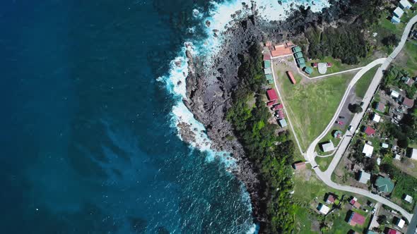 Overhead drone shot of azure sea, black coast and rooftops on the coast in Saint Kitts and Nevis