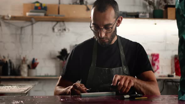 A man of Arab appearance sharpens a blade in a workshop. Sculptor, painter, needleworker.