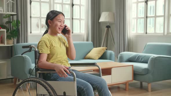 Asian Kid Girl Sitting In A Wheelchair And Talking On Phone At Home