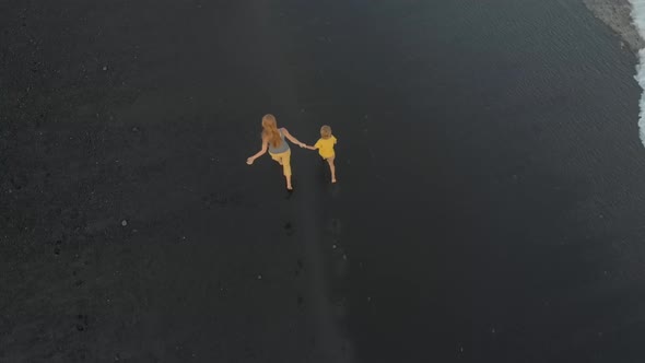 Aerial Shot of a Mother and Her Son Walking and Having Fun on a Beach with a Black Volcanic Sand