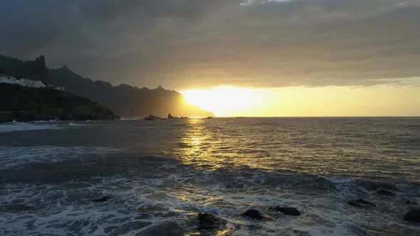 Flight Above Ocean Waves Facing Beautiful Sunset and Mountains on Horizon. Aerial Drone Shot of