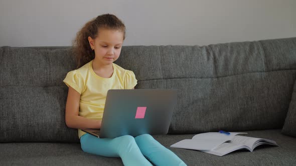 Cute Primary School Child Girl Studying with Laptop at Home Sit on Sofa