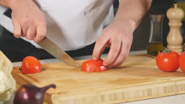 Close-up Shot of a Person Cutting Tomato with Sharp Knife on a Wooden Board