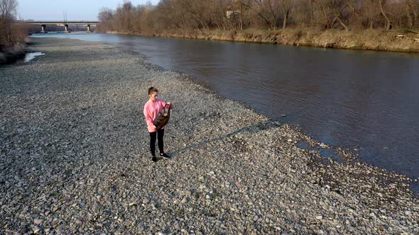 Young woman with her son collects plastic garbage in a garbage bag on the river