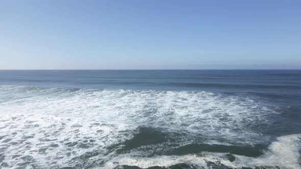 Rolling waves breaking near shore, looking out at a clear horizon, aerial dolly