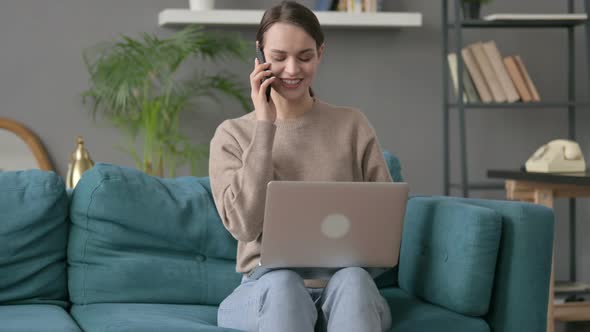 Woman with Laptop Talking on Smartphone on Sofa