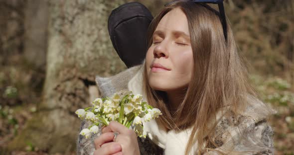 the girl sniffs a bouquet of white flowers in a ray of sunshine then smiles and looks at the camera