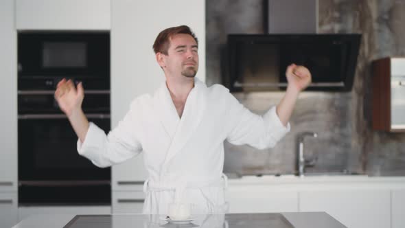 Handsome Man in Bathrobe Yawning and Stretching at Kitchen Enjoying Cup of Coffee in Morning