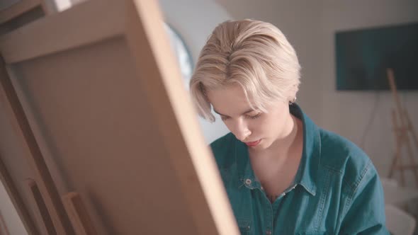 A Young Blonde Woman Artist Draws a Painting in the Art Studio