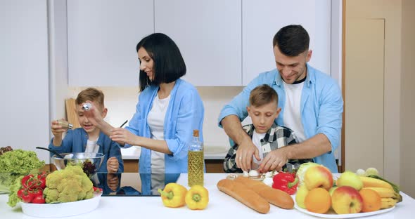 Parents Cooking Vegetable Salad Together with Joint Children on Modern Kitchen