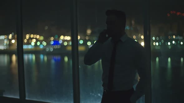 Businessman Talking on Phone by Window at Night