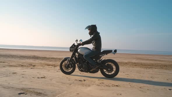 Motorcyclist Driving His Customized Fast Motorbike on the Dirt Road in Desert Around Sea or Lake