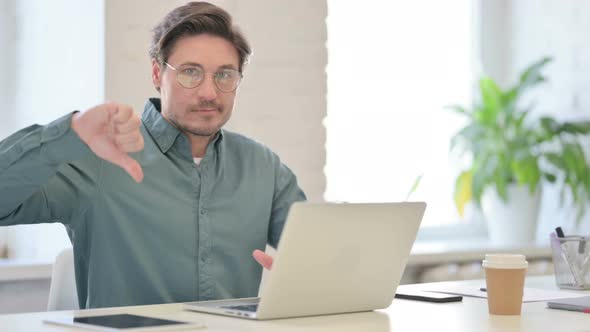 Thumbs Down By Middle Aged Man with Laptop in Office